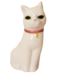 a white ceramic cat with black eyes, green eyeliner, and a red collar with a yellow bell around it's neck.